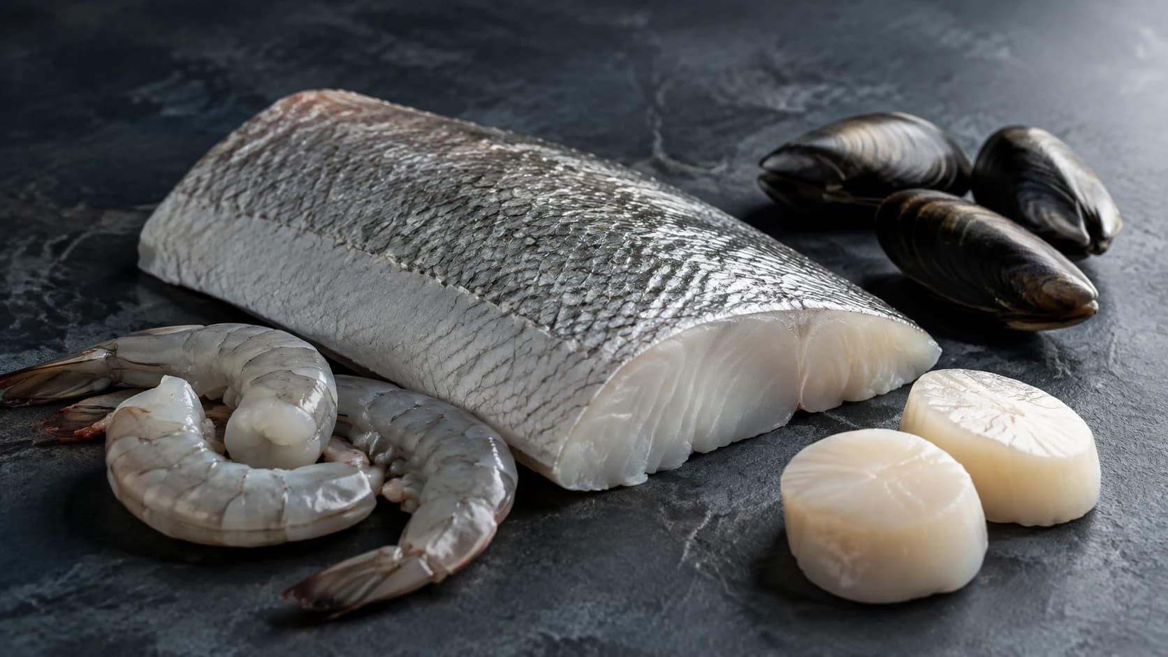 Fish fillet and shellfish arranged on dark stone